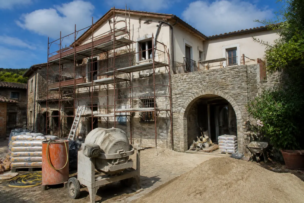 Casa in pietra con ponteggi esterni e materiali per ristrutturare casa in cortile.